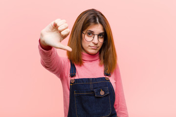 young pretty woman feeling cross, angry, annoyed, disappointed or displeased, showing thumbs down...