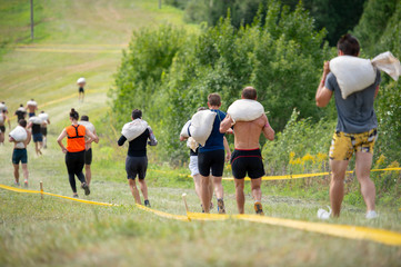 Group of people running crossover with heavy bags on their shoulders in summer sunny day