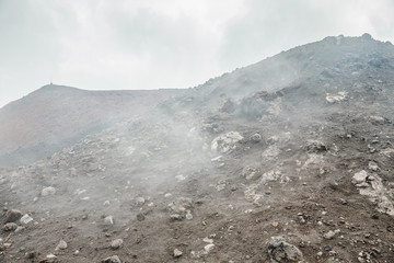 Top of crater Mount Etna volcano, frozen cold lava smokes, thick clouds