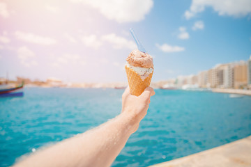 Man holds ice cream in cone with spoon against blue sea. Relaxation concept