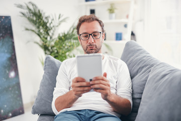 Man using tablet and sufring on the internet in his living room.