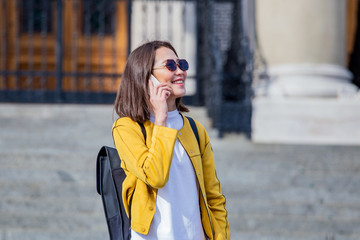 Fototapeta premium Portrait of a young, attractive and beautiful Asian woman smiling as she talks on her smartphone int he city. She is looking away as she talks animatedly and happily on her mobile device.