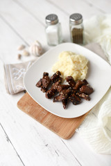 Sesame beef dish on a white wood background served with mashed potatoes and seasonings