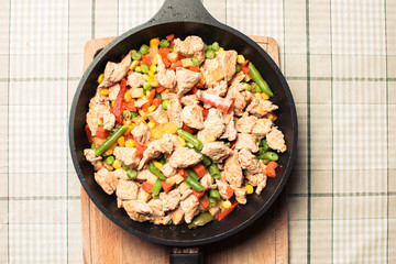 Fried tender chicken pieces with vegetable mixture in pan on wooden board.