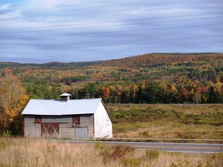 Old gray and red barn with autumn colors on the hills behind