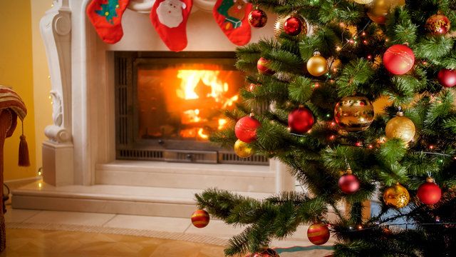 Beautiful image of Christmas tree with lights and baubles against burning fireplace at living room