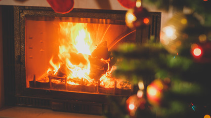 Beautiufl toned image of burning fireplace next to decorated Christmas tree with baubles and...