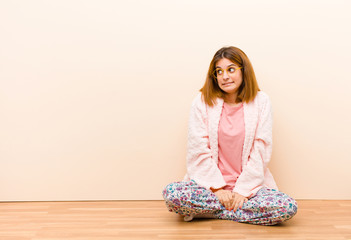 young woman wearing pajamas sitting at home looking worried, stressed, anxious and scared,...