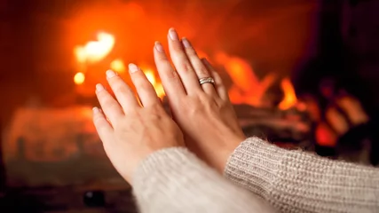 Foto op Plexiglas Closeup image of young woman in sweater warming her hands at burning fireplace at house © Кирилл Рыжов