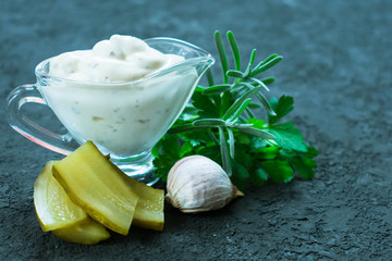 Tartar sauce in a glass gravy boat with ingredients on a black background. Close-up.