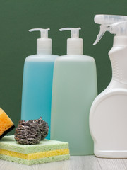 Bottles of dishwashing liquid, glass and tile cleaner and sponges on green background.