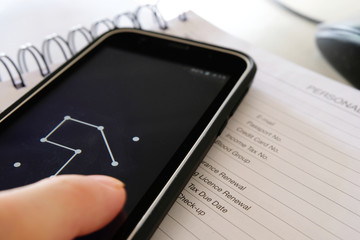 Smarphone on personal detail page of a diary as a hand draws a pattern lock password to unlock the...