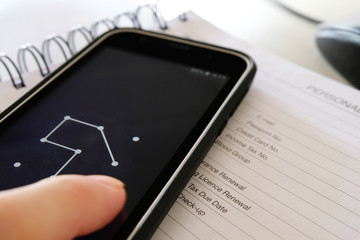 Smarphone on personal detail page of a diary as a hand draws a pattern lock password to unlock the phone. Like a diary, the smartphone now contains many personal details requiring security protection.
