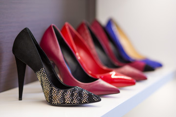Women's shoes in the store. Shoes of different colors presented on the trading shelf. A collection of high-heeled shoes standing on a shelf in a store.