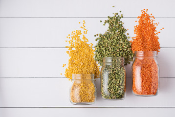 Three jar with yellow, orange and green  lentil scatter on white wooden  table. Image is top view...
