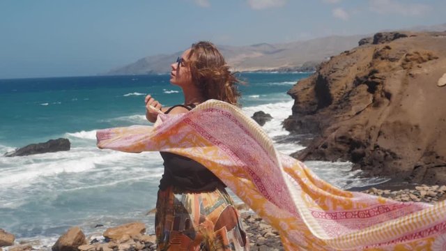 Beautiful young woman girl holding fabric pareo sarong at wind in a summer vacation, sea and mountains view, freedom concept. Tourist on islands