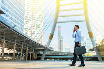Young business man walking and talking on the mobile with city background.