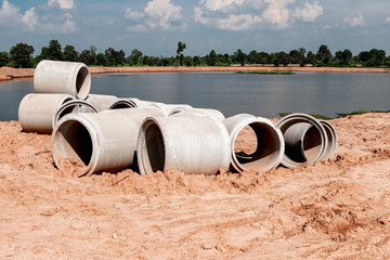 Large cement pipes on the ground to wait for installation under the soil. Riverside in the countryside of Thailand.