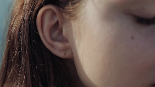Beautiful girl inserts headphones into ears, good mood, close-up, outdoors