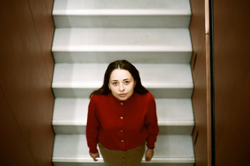 A brunette with long hair in a red sweater stands on a white staircase and looks from below