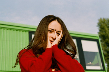 brunette stands against the sky and looks at the camera covering her face with her hands