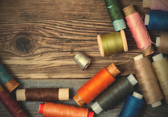 thimble and spools of thread on an aged wooden surface - obrazy, fototapety, plakaty