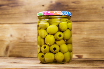 Pickled green olives in glass jar on wooden table