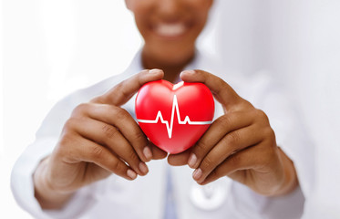 health, medicine and charity concept - african american female doctor holding red heart with ecg...