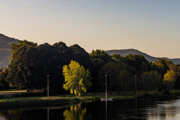 small sailling boat on river banks with mountains in background at sunset