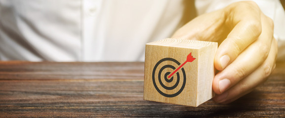 A businessman holds in his hands a wooden block with a target symbol. The concept of achieving...