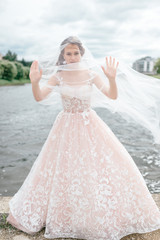Fototapeta na wymiar Beautiful bride in wedding dress with veil over her face posing outdoor with lake on background.