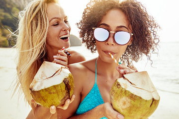 Two laughing young women sipping on coconuts at the beach