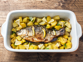Baked fish carp with potatoes in a ceramic pan. Rustic style.