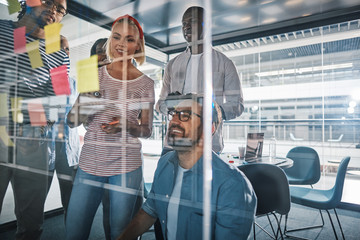 Smiling businesspeople brainstorming on the glass wall of a boar
