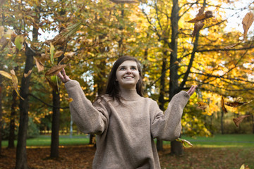 Uśmiechnięta dziewczyna podrzuca liście w parku.