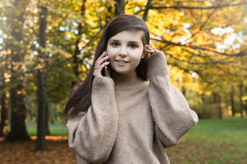 Dziewczyna rozmawia przez telefon. Kolorowe drzewa w tle. 