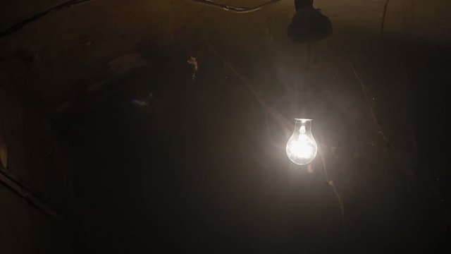 Close-up ordinary electric lamp hanging and swinging in dusty and smoky rusty and dirty basement bunker, like bomb shelter, huge spider web in foreground