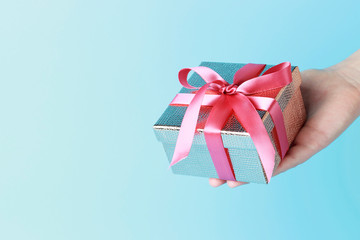 Female hand holding gift box with ribbon on blue background