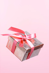 Gold color gift box with ribbon on pink background close-up. Levitation