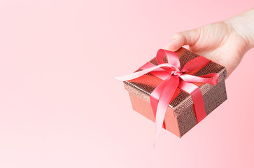 Female hand holding gift box with ribbon on pink background, copy space