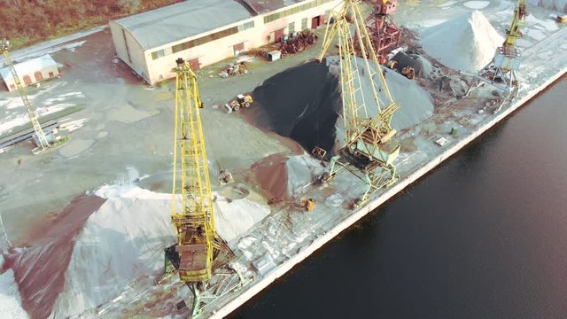 port cranes on the river bank produce sand. Port cranes with a bucket on the river bank. Extraction of river sand. Port cargo cranes extracts river sand, production. Sunset. Barge.
