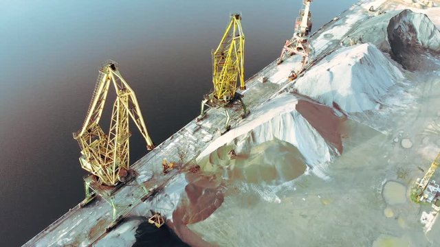 port cranes on the river bank produce sand. Port cranes with a bucket on the river bank. Extraction of river sand. Port cargo cranes extracts river sand, production. Sunset. Barge.