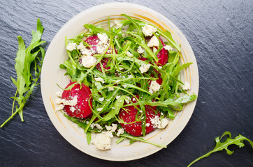 Top view at clay dish with beetroot arugula and feta cheese salad on slate stone tray closeup view