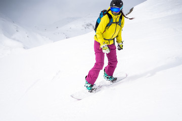 Fototapeta na wymiar Sporty woman in helmet and mask snowboarding on snowy slope.