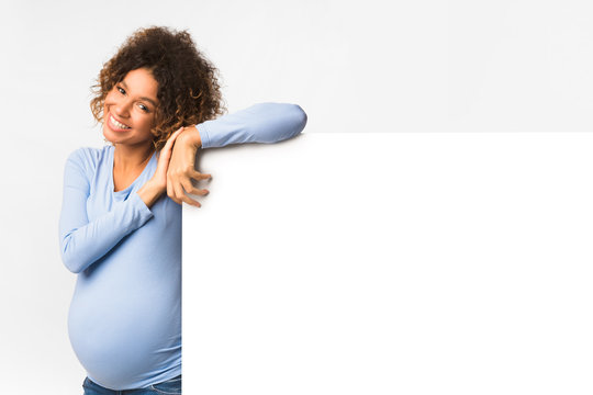 Happy black pregnant woman with billboard, light background