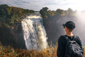 Tourist looks at the Victoria Falls on Zambezi River in Zimbabwe - obrazy, fototapety, plakaty