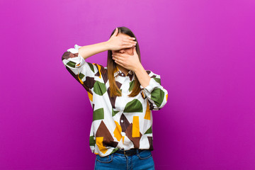 young pretty woman covering face with both hands saying no to the camera! refusing pictures or...