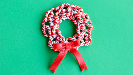 red and white multiple candy cane wreath with a red bow laying on a green color background with writing space