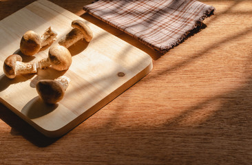 Mushrooms arranged on a wooden cutting board on wood table and black background by the window with morning sun light, Is a diet that has many vitamins and fiber, Is a popular food among vegetarians.