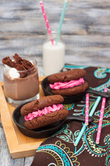 Chocolate sandwich cookies with pink butter cream in black iron mini skillets. Bottle of milk and glass of milkshake with marshmallows on the background.